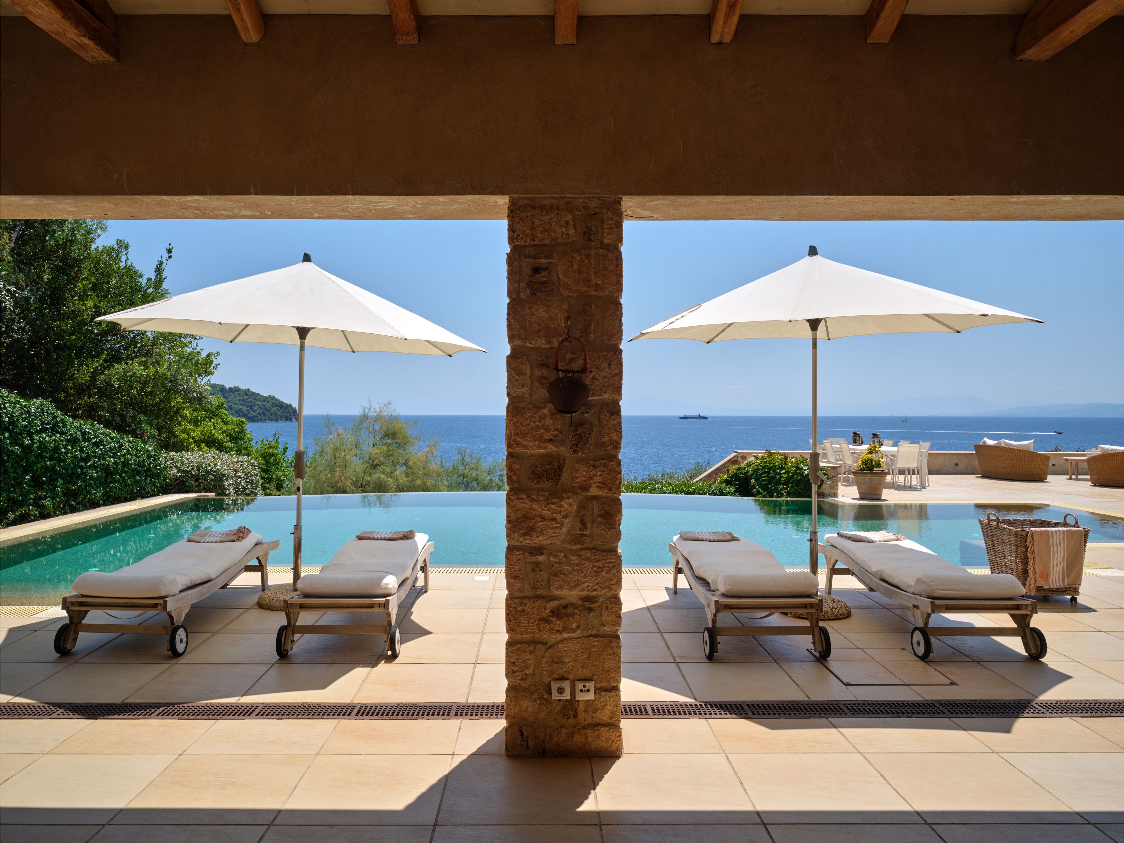 Sunbeds under the umbrellas beside the infinity pool, seen from the covered terrace