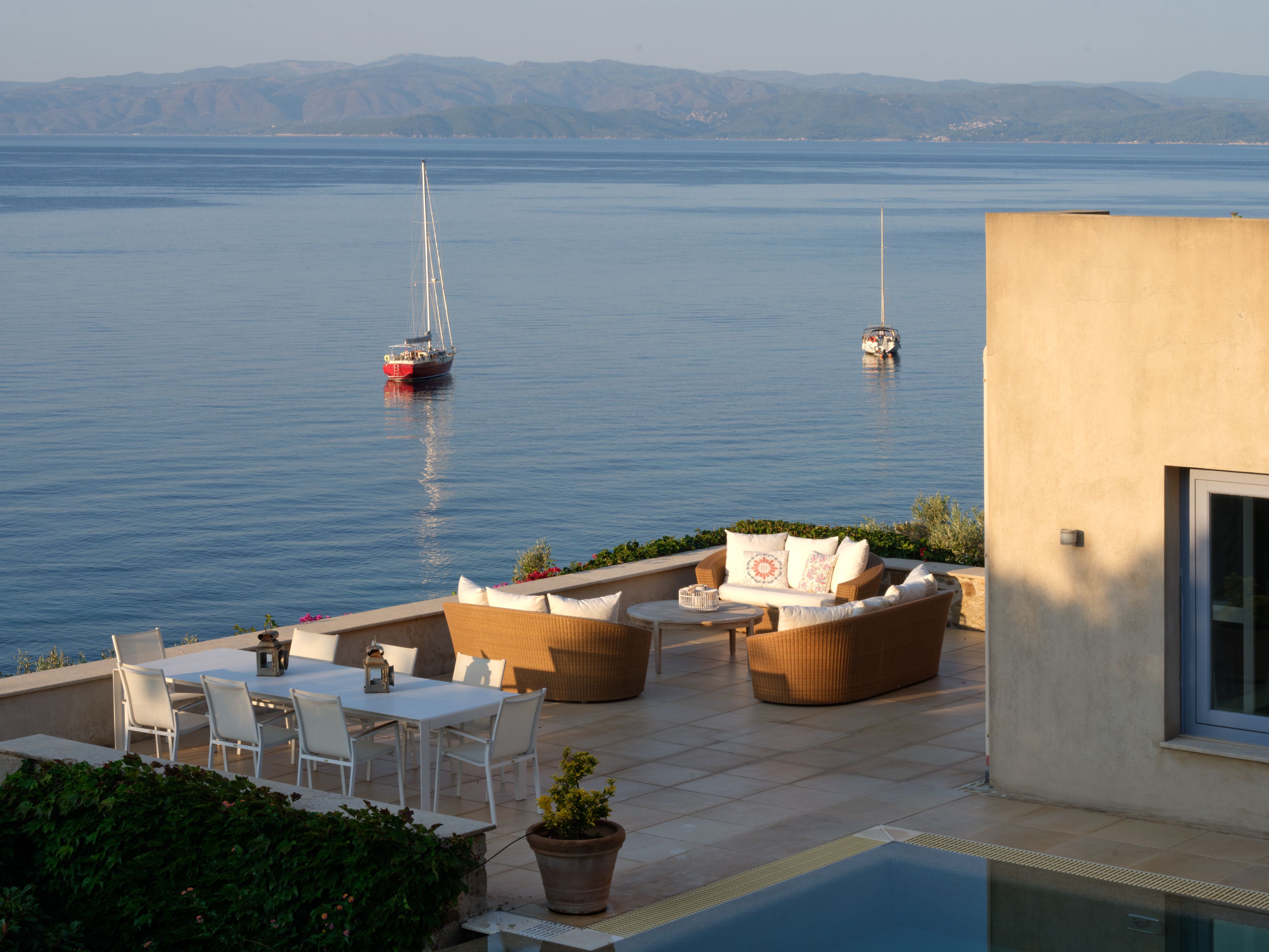 Outdoor sofas on the pool terrace, with yachts at anchor in the bay